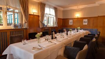A long dining table set for a formal meal, with chairs and a view of the outdoors through large windows.
