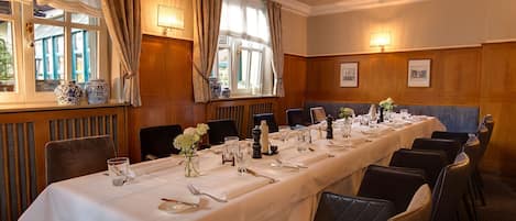 A long dining table set for a formal meal, with chairs and a view of the outdoors through large windows.