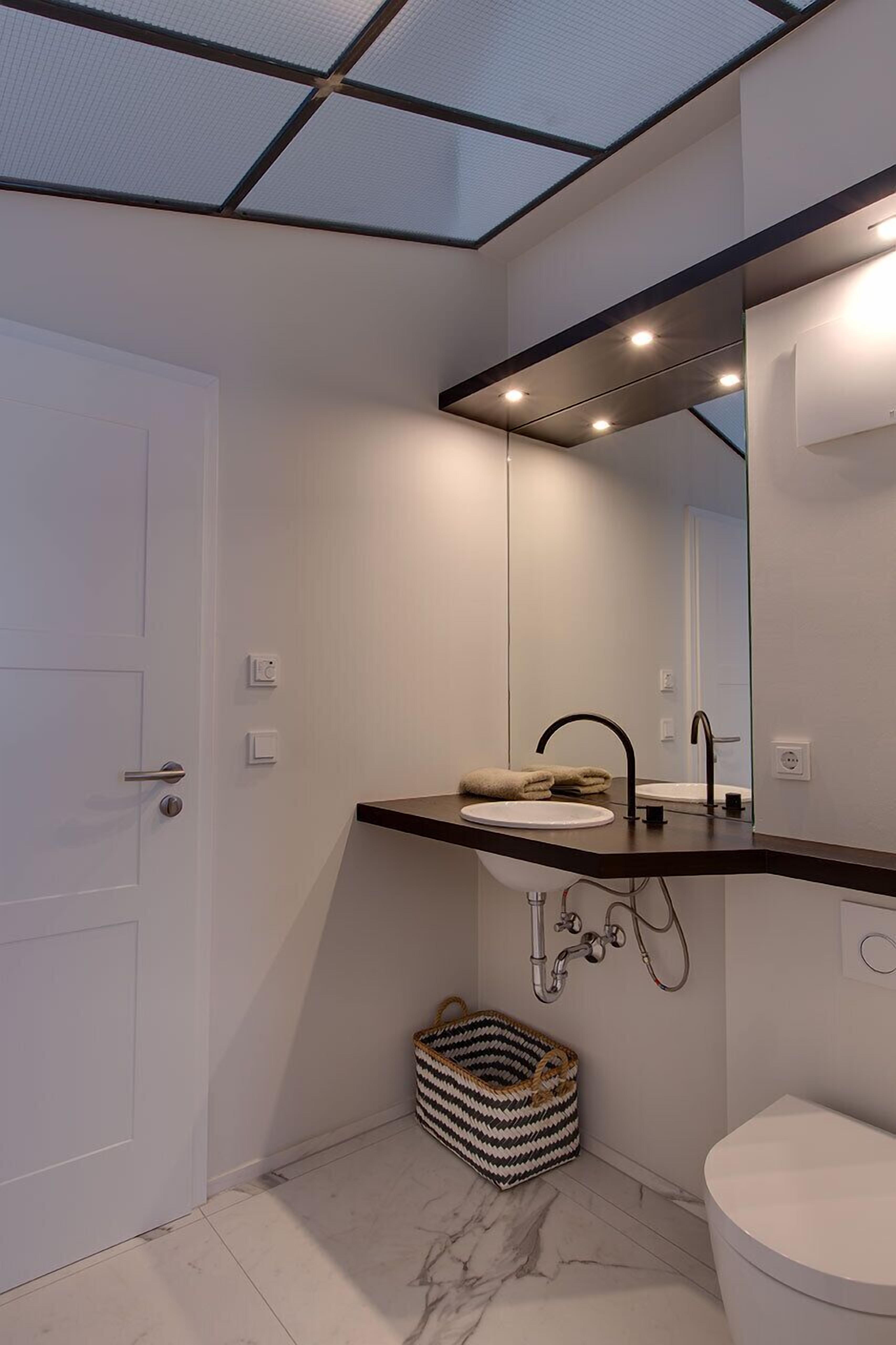 A modern bathroom with a white door, a large mirror, a sink with a towel, and a toilet.