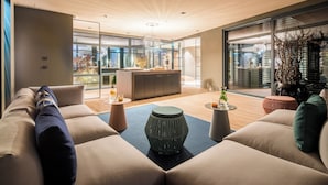 A modern living room with a sofa, a coffee table, and a decorative stool. There is a glass partition with a view of the outside. - Zeller Hotel & Restaurant (Kahl)