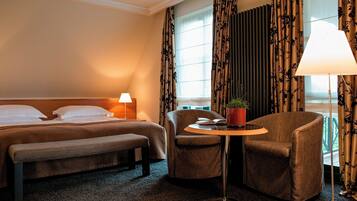 Ein Hotelzimmer mit einem Bett, einer Bank, einem Stuhl, einem kleinen Tisch mit einer Pflanze und einer Lampe.