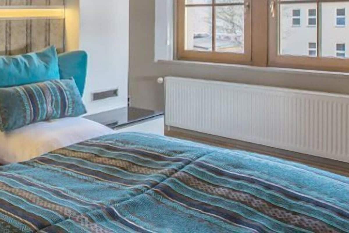 A bedroom with a bed, pillows, a nightstand, a window, and a radiator.