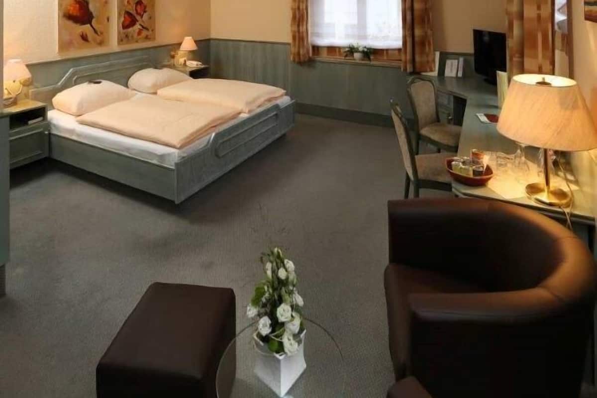 A hotel room with a bed, a desk, a chair, and a small table with a vase of flowers.