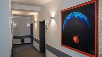 A hallway with a painting of a blue planet and an apple, a potted plant, and a door with an elevator.