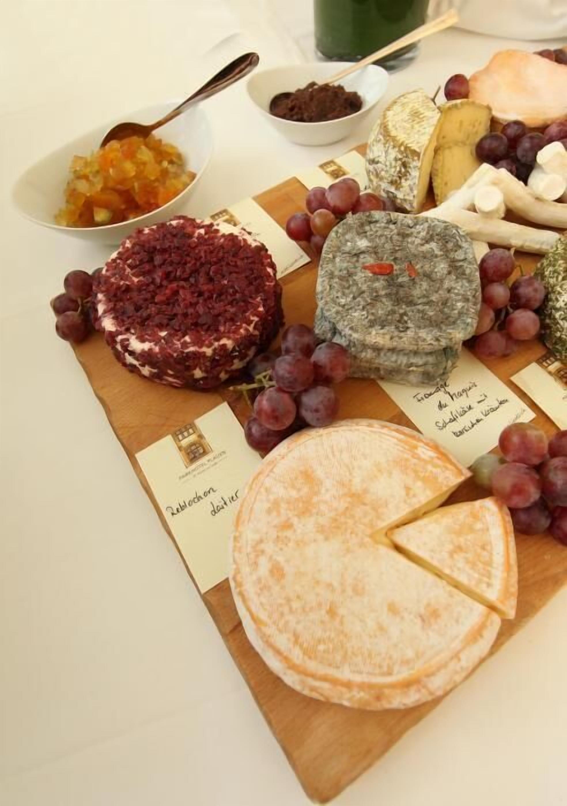 Tábua de queijos com diversos tipos de queijo, uvas e uma tigela de frutas.