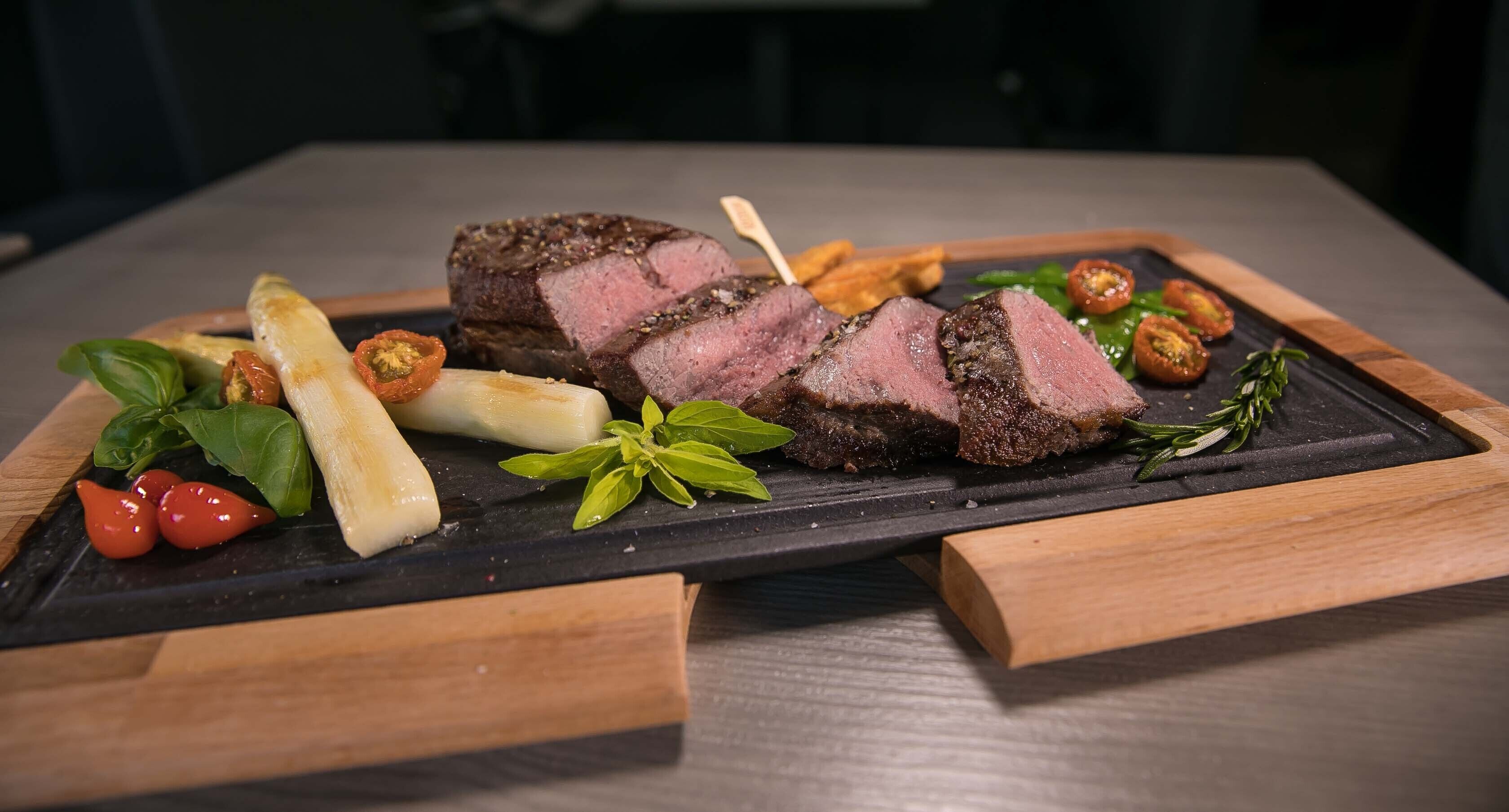 Una tabla de pizarra negra con filete en rodajas, tomates cherry, albahaca y cebollas encurtidas.