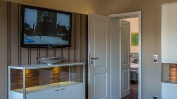 A modern living room with a flat-screen TV mounted on the wall, a glass-top coffee table, and a wooden floor.
