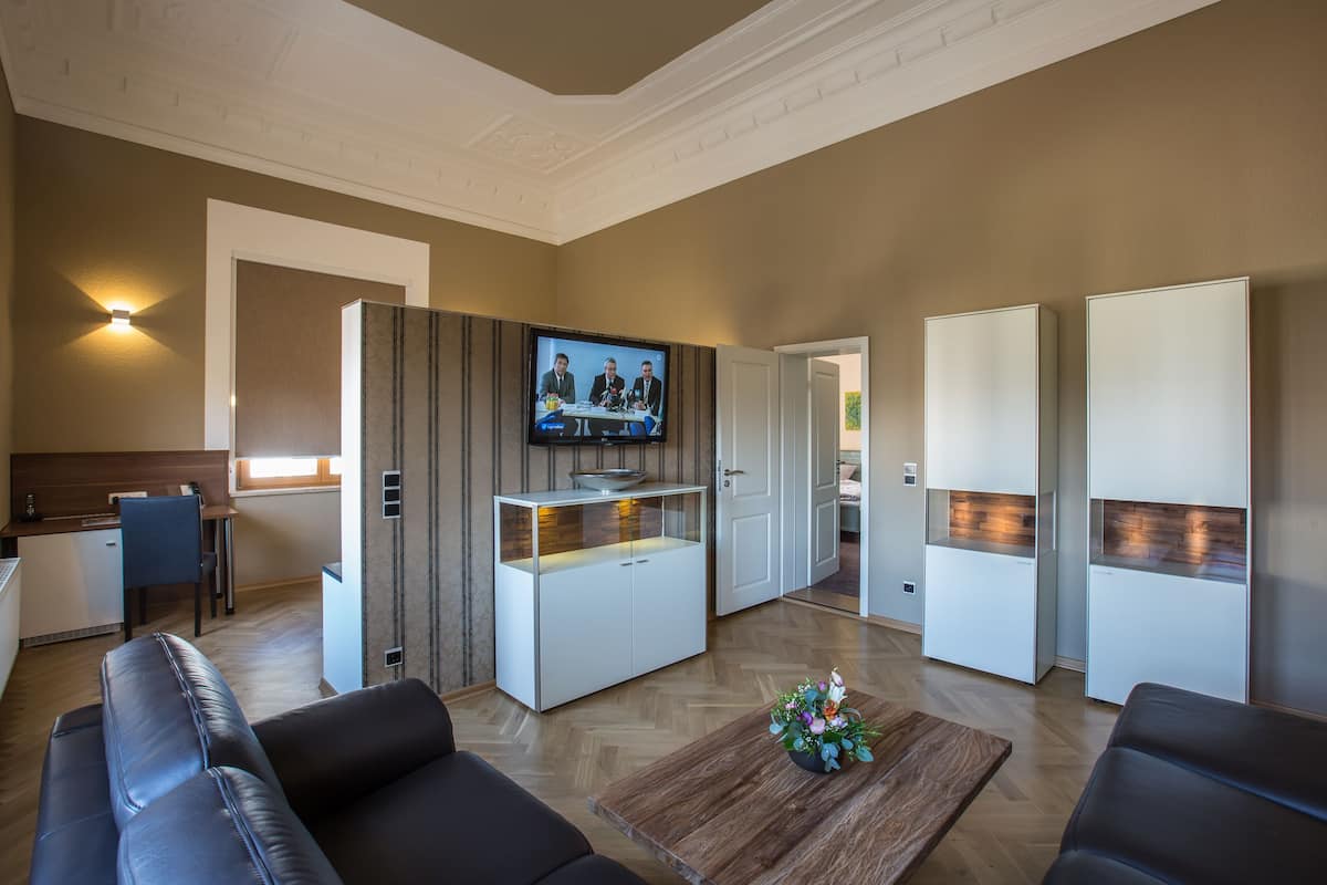 A modern living room with a flat-screen TV, a wooden coffee table with a floral centerpiece, and a seating area with leather sofas.
