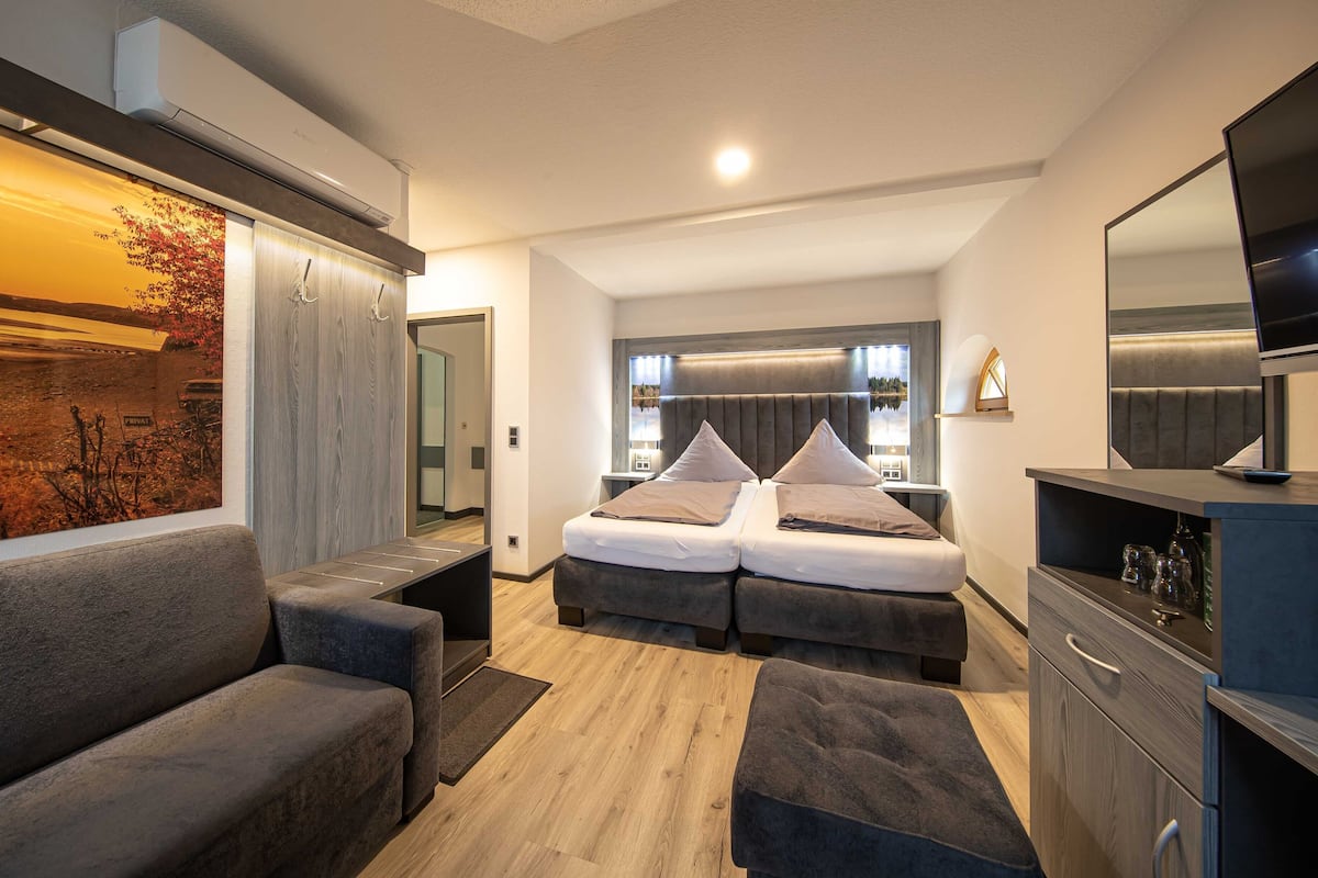 A modern bedroom with a double bed, a sofa, a TV, and a large window.