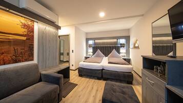 A modern bedroom with a double bed, a sofa, a TV, and a large window.