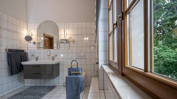 A modern bathroom with a double sink, a large mirror, and a window providing a view of greenery outside.