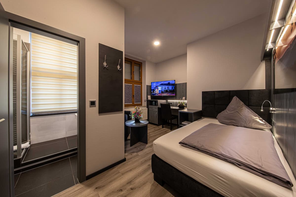 A modern hotel room with a bed, a desk, a television, and a small kitchenette.