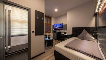 A modern hotel room with a bed, a desk, a television, and a small kitchenette.