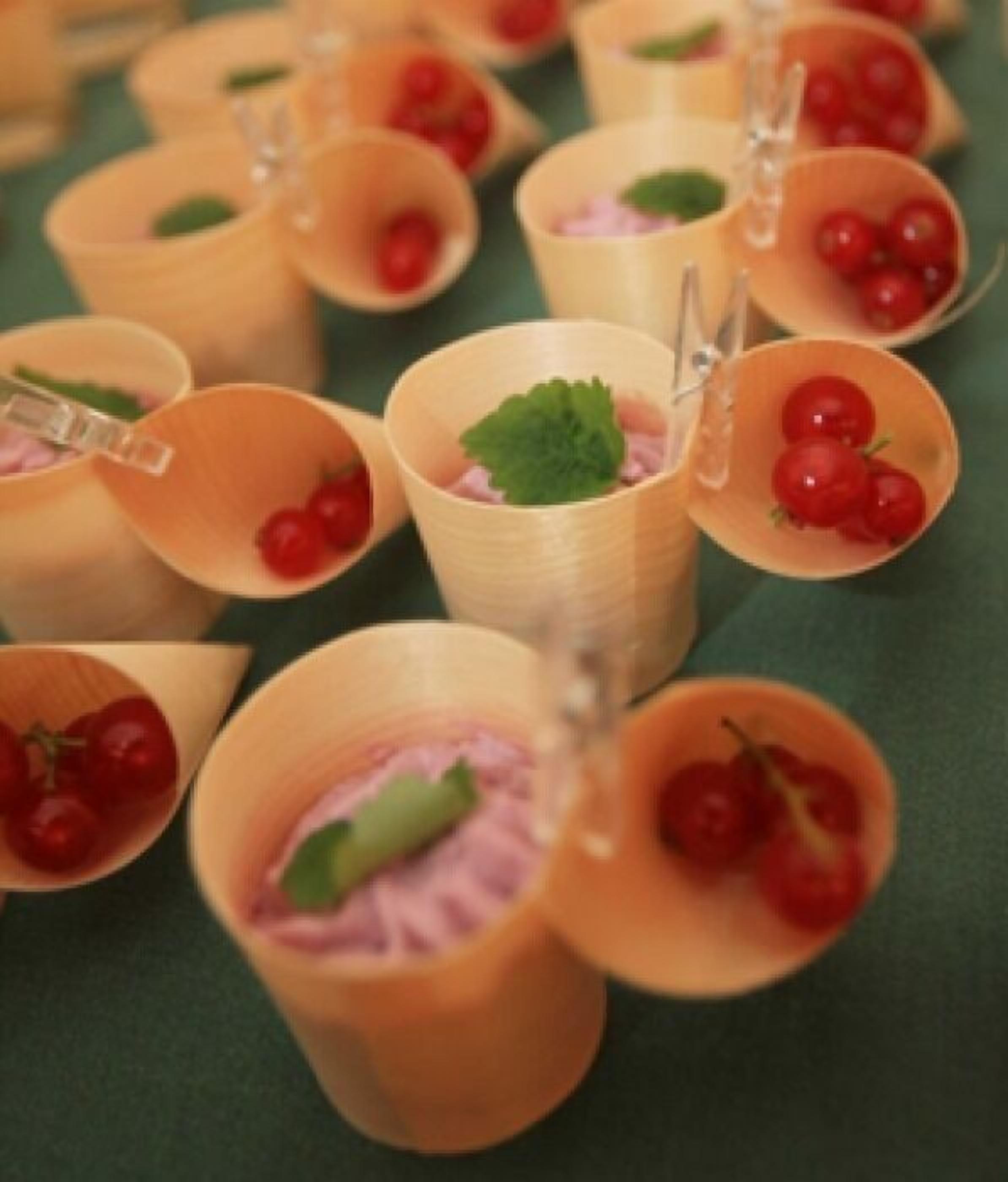 A row of wooden cups with cherry tomatoes and mint leaves.