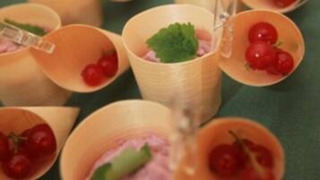 A row of wooden cups with cherry tomatoes and mint leaves.