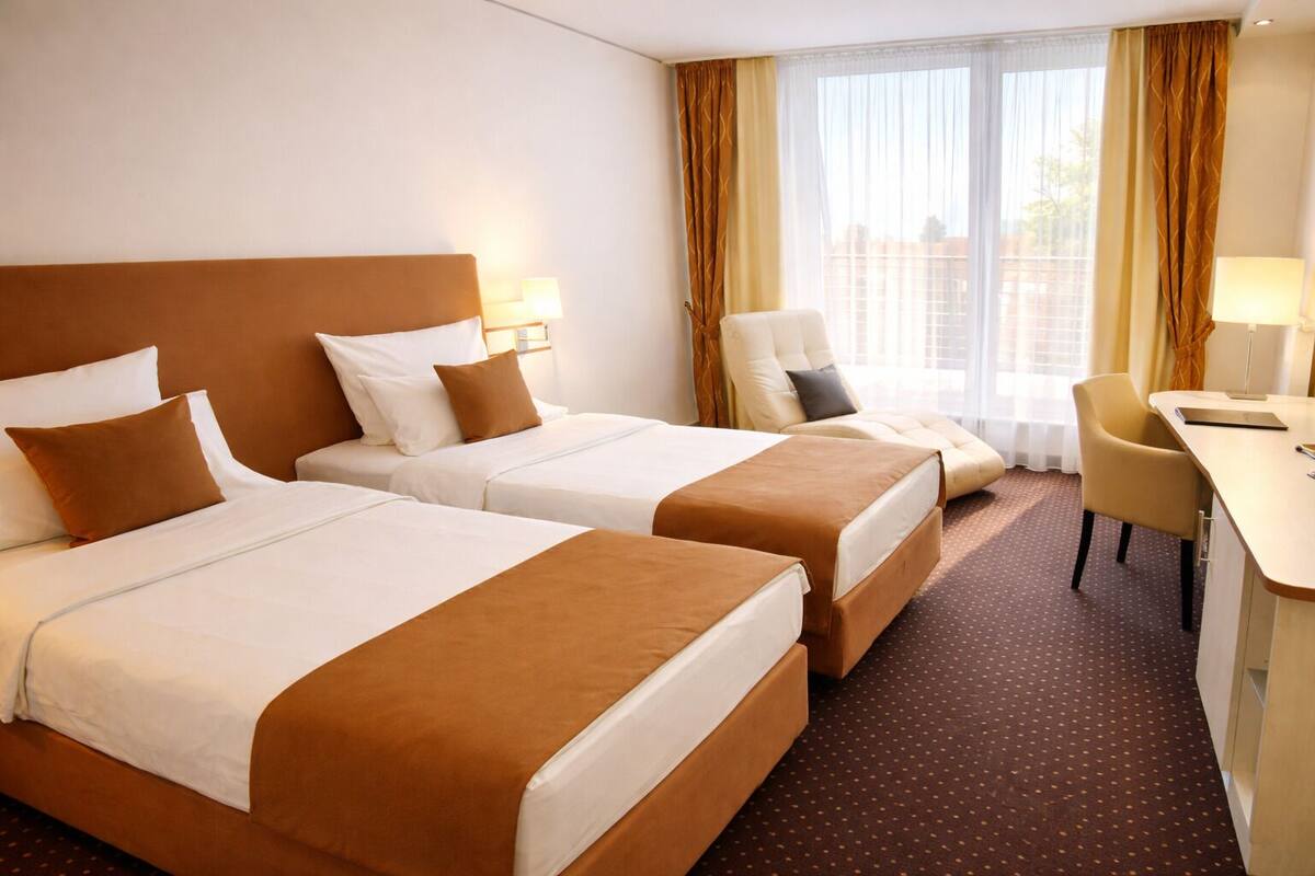 A hotel room with two beds, a desk, a chair, and a window with curtains.