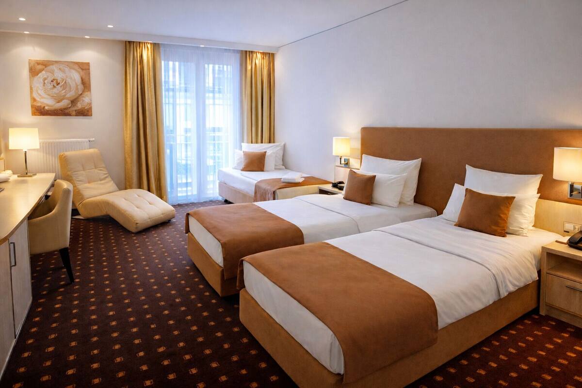 A hotel room with two beds, a desk, a chair, and a large window with curtains.