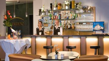 Un espace bar comprenant un comptoir, des étagères remplies de bouteilles et de verres, ainsi qu’une table avec des chaises.