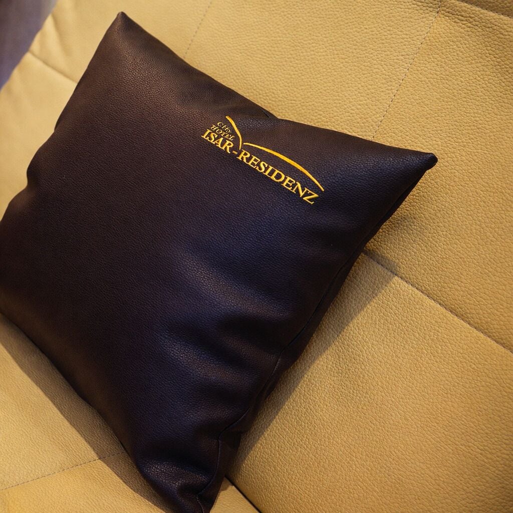 A dark-colored pillow with a logo on a beige leather couch.