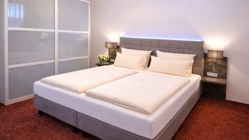 A double bed with a grey headboard, two bedside tables with lamps, a large window with frosted glass panels, and a red carpeted floor.