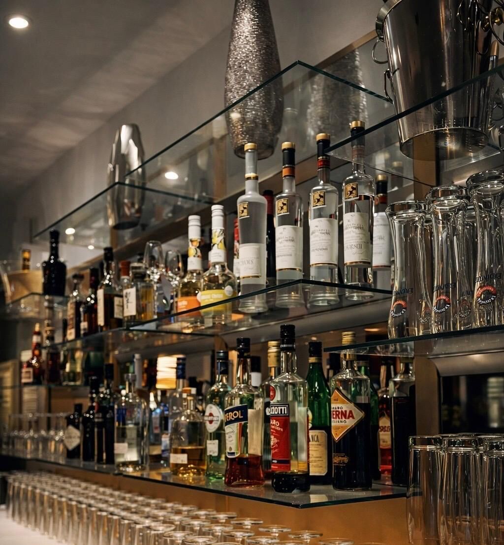 Zona de bar con estantes llenos de botellas de licores y vasos.