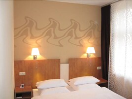 Una habitación de hotel con dos camas, mesitas de noche y lámparas fijadas a la pared.