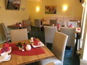 A dining area with tables and chairs, a painting on the wall, and a mirror reflecting part of the room.