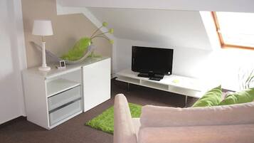 Ein modernes Wohnzimmer mit Flachbildfernseher, weißem Schreibtisch, Lampe und einer Zimmerpflanze.