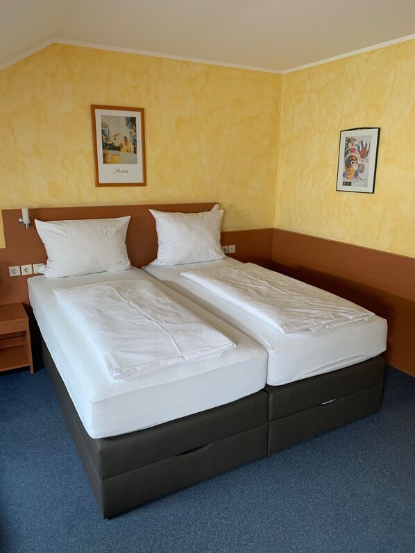 A double bed with white linens, a wooden headboard, and a brown bedside table.