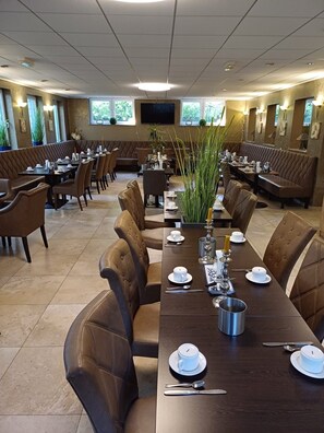 A restaurant with a long dining table set for a meal, surrounded by booths and chairs. - Hotel Nord (Rheinbach)