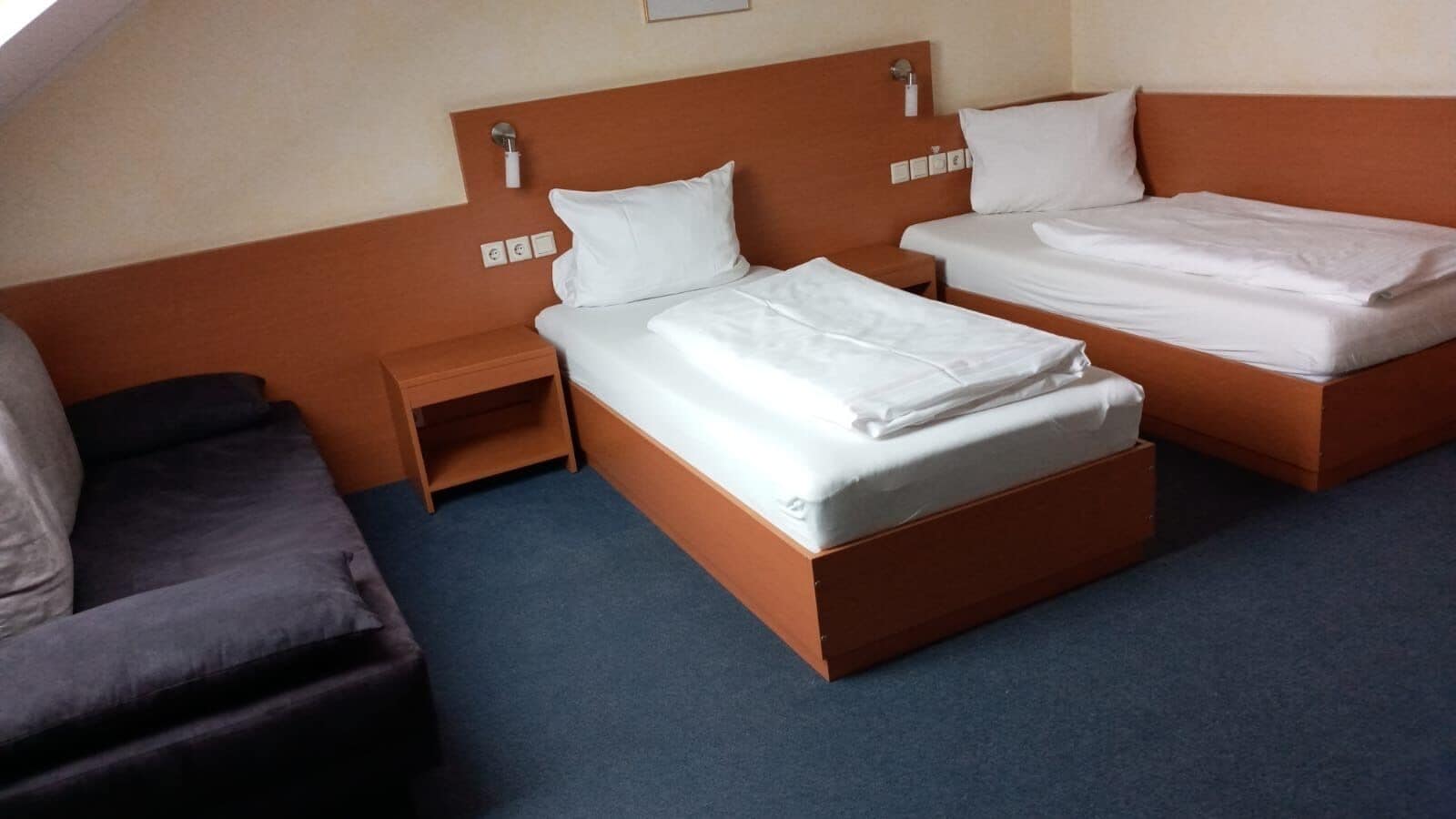 Et hotelværelse med to senge, et trænatbord, et lille bord og en mørk sofa.