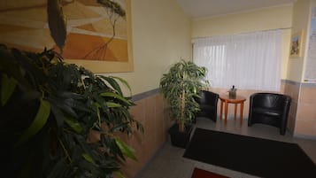 Un hall con una planta grande en maceta, dos sillones de cuero negro, una mesita redonda con planta y una alfombra roja en el suelo.
