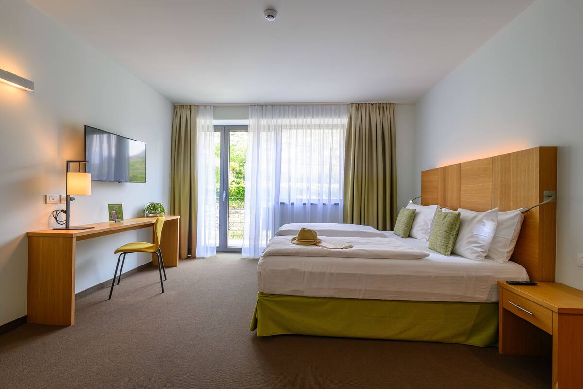 Een hotelkamer met een bed, bureau, stoel en een televisie aan de muur.