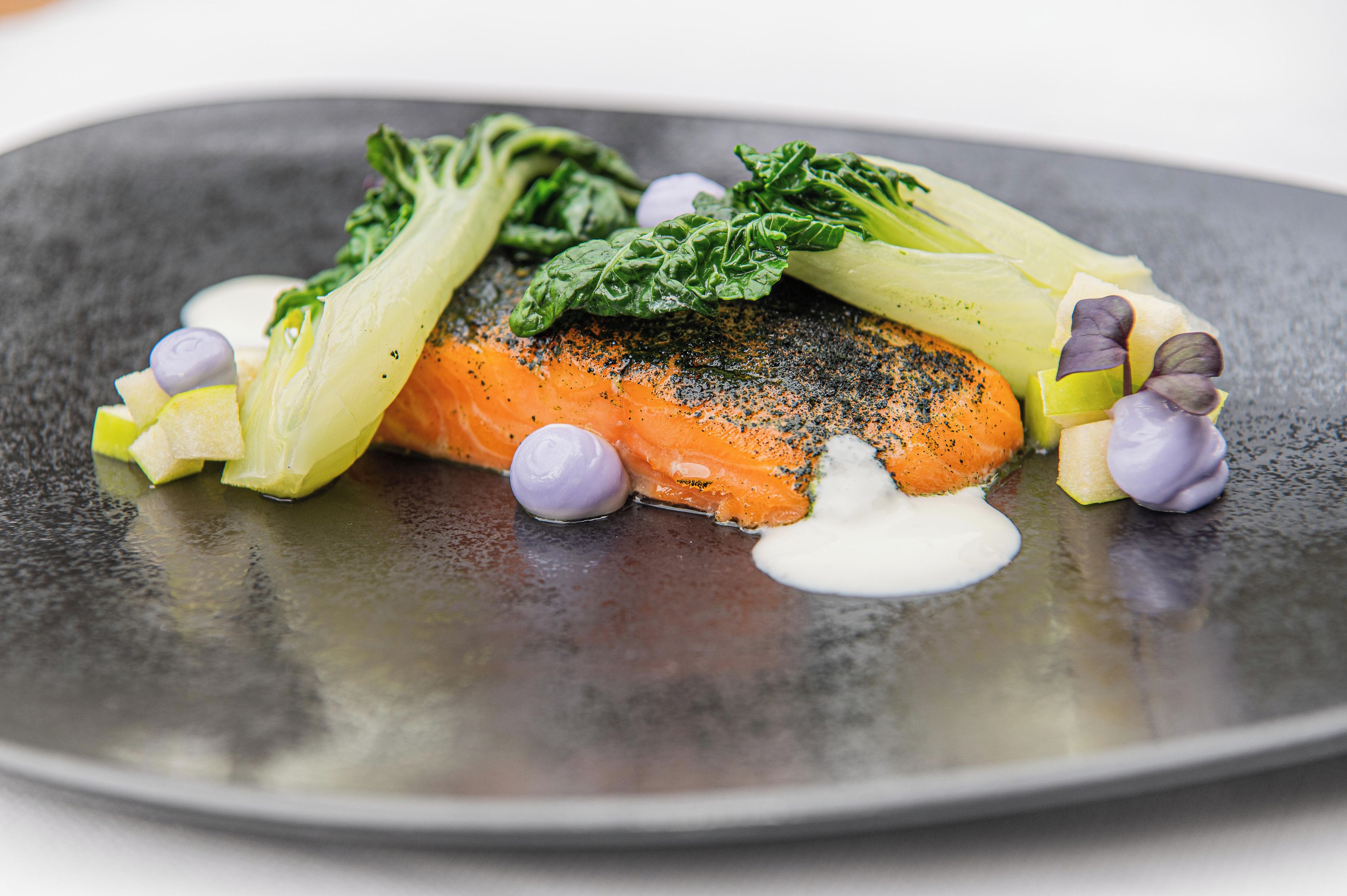 A plate with a piece of salmon, greens, and purple elements.