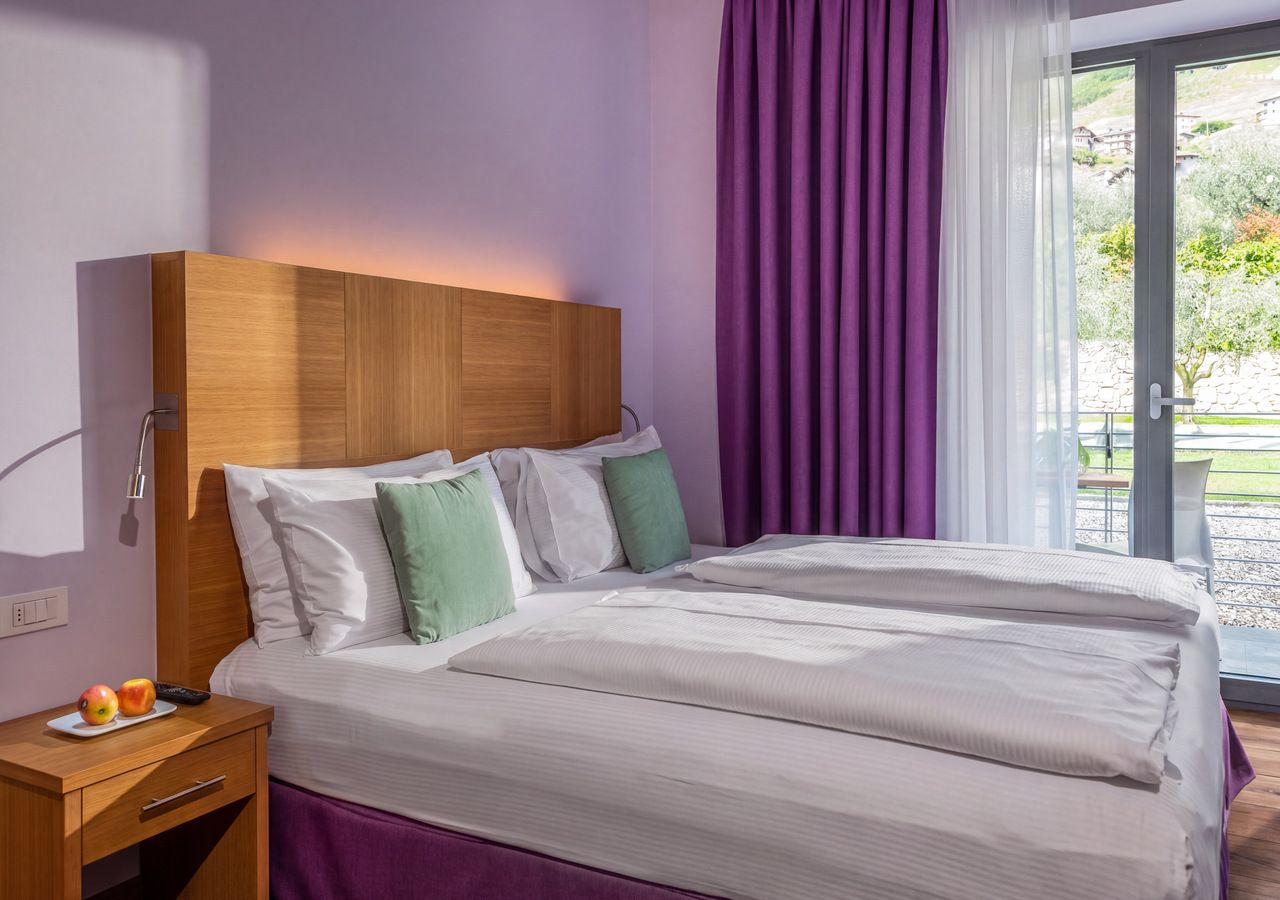 Una habitación de hotel con cama, mesita de noche y ventana con cortinas.