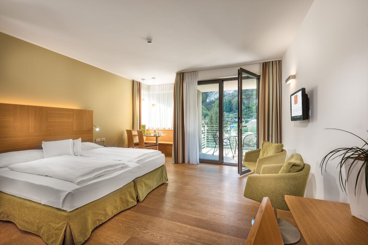 Hotelkamer met een groot bed, een bureau, een stoel en een balkon met uitzicht op de bergen.