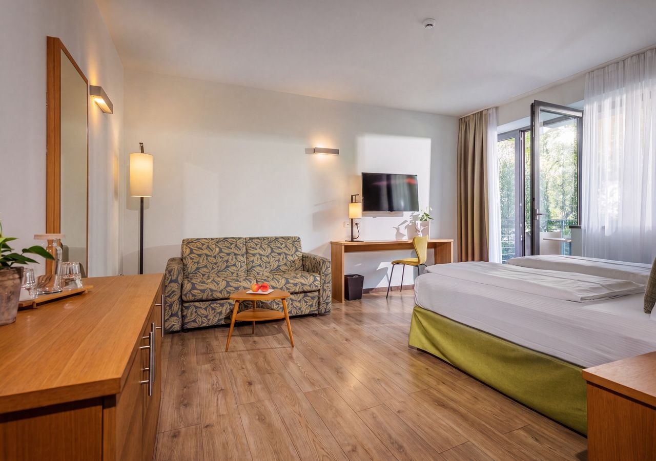 Ein Hotelzimmer mit Bett, Sofa, Schreibtisch und Fernseher.
