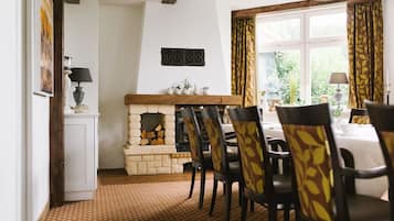 A dining area with a fireplace, wooden beams, and patterned chairs.