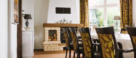 Un comedor con chimenea, vigas de madera y sillas estampadas.