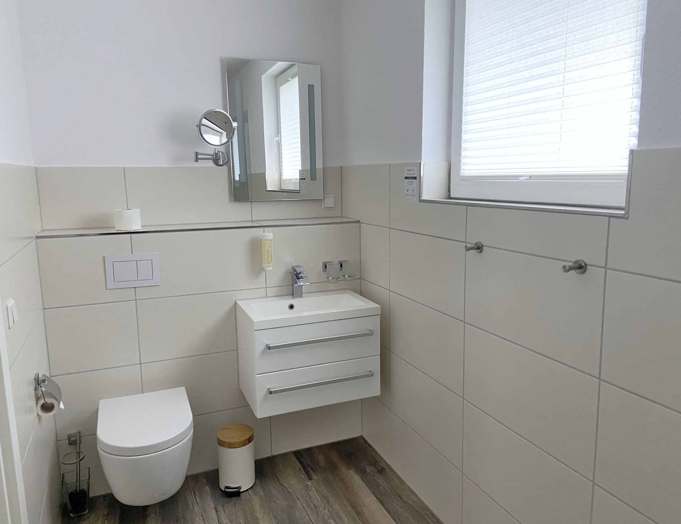Une petite salle de bain moderne, équipée de toilettes, d’un lavabo, d’un miroir et d’une fenêtre.
