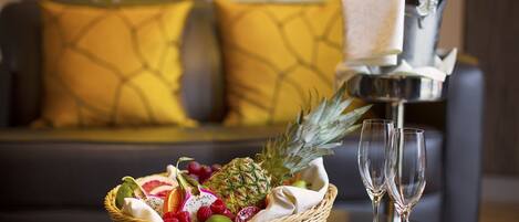 A fruit basket with a pineapple and grapes on a table, two champagne flutes, and a bottle of champagne in a silver bucket.