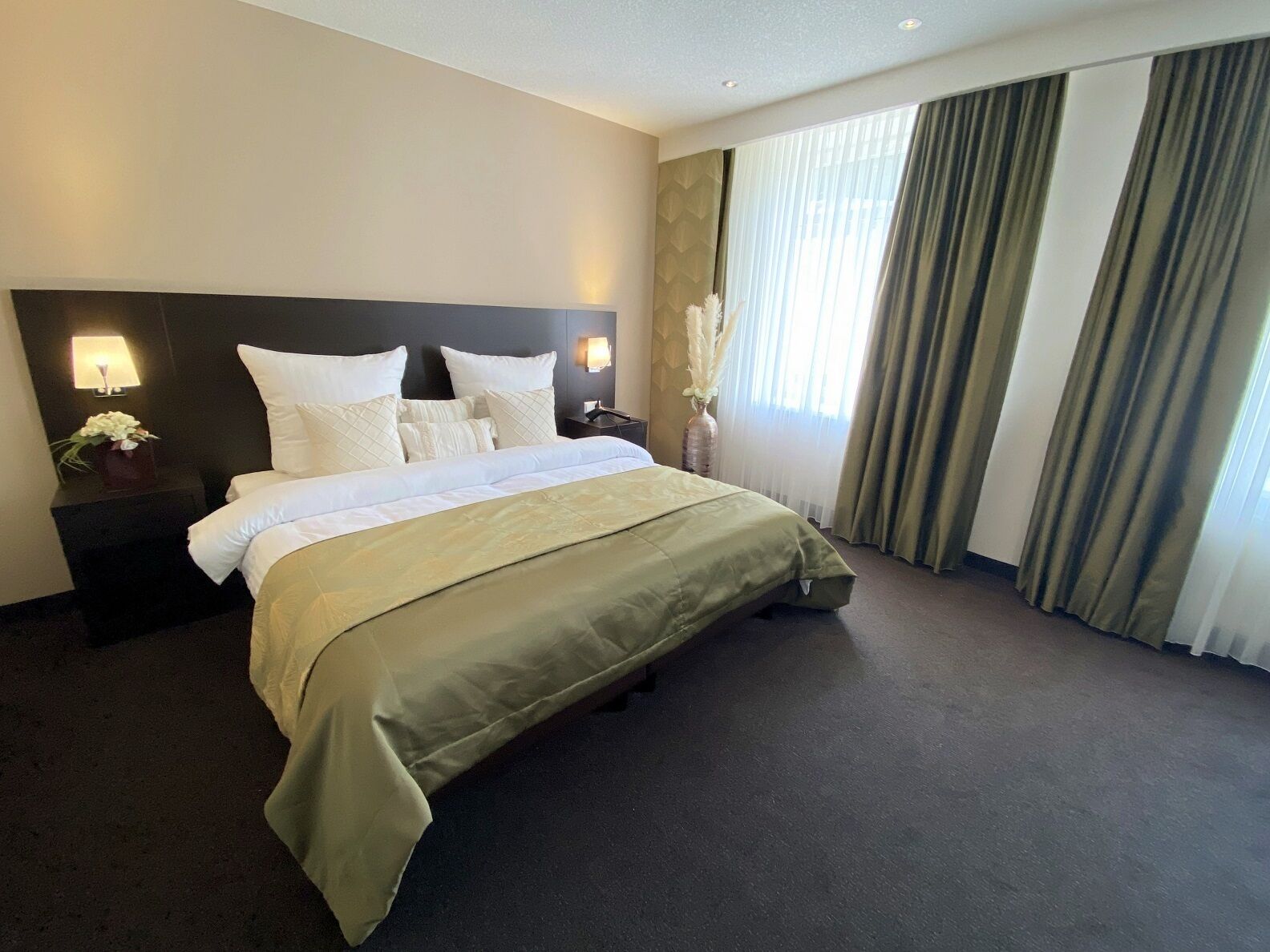 A hotel room with a large bed, a nightstand with a lamp, and a vase with flowers.