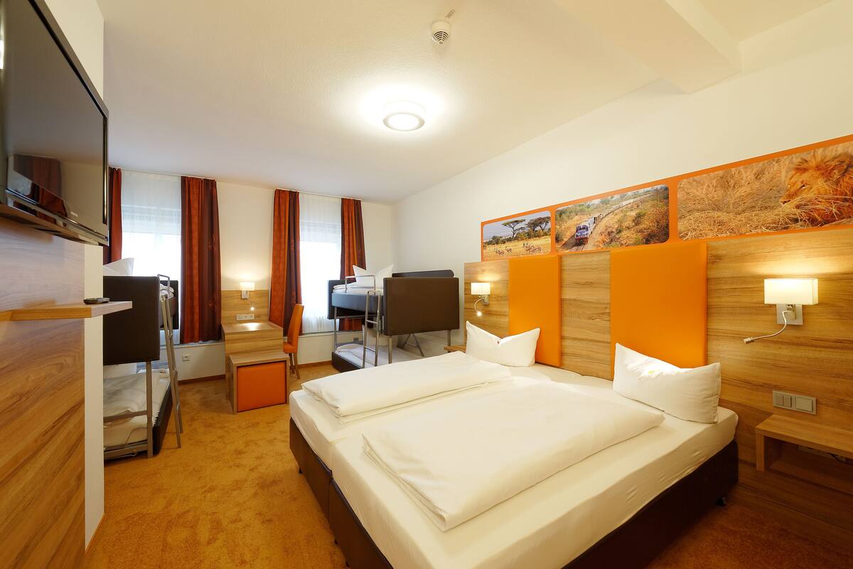 A hotel room with two beds, a desk with a chair, a TV, and artwork on the wall.