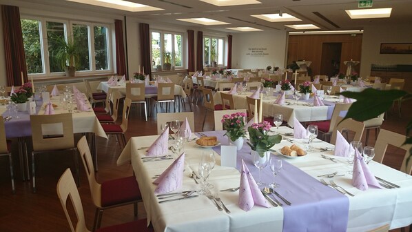A banquet hall with multiple tables set for dining, featuring white tablecloths and purple napkins.