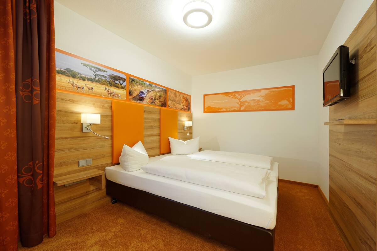 A hotel room with a bed, wooden headboard, wall-mounted TV, and artwork depicting wildlife.