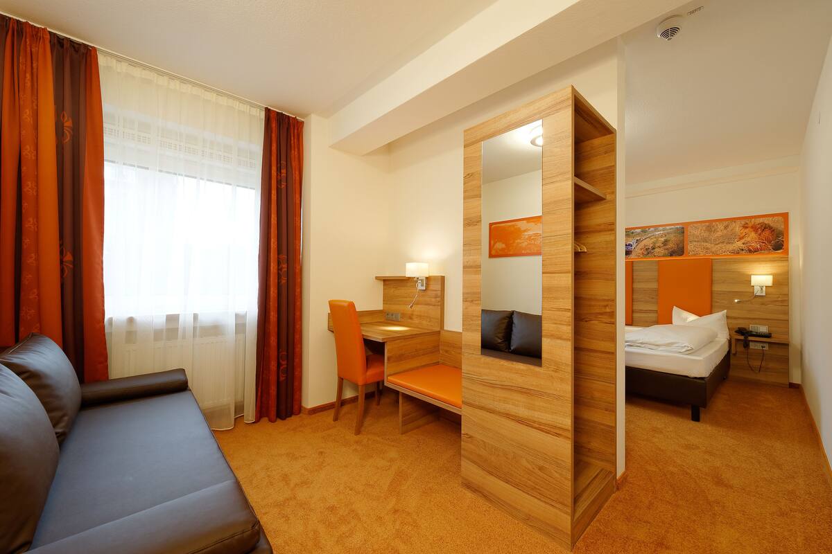 A hotel room with a sofa, a desk with a chair, a bed, and a large mirror.