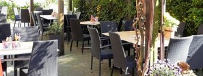 An outdoor dining area with wicker chairs and tables, surrounded by greenery and potted plants. - Hotel Gasthof Zur Post (Leipheim)