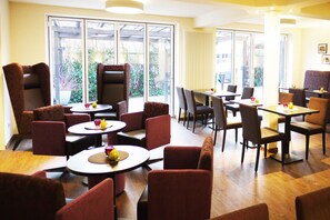 A hotel dining area with round tables and chairs, large windows, and a view of the outdoors.