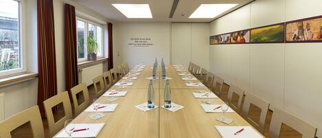 Un salón de conferencias con una larga mesa, sillas y una pared decorada con obras de arte.