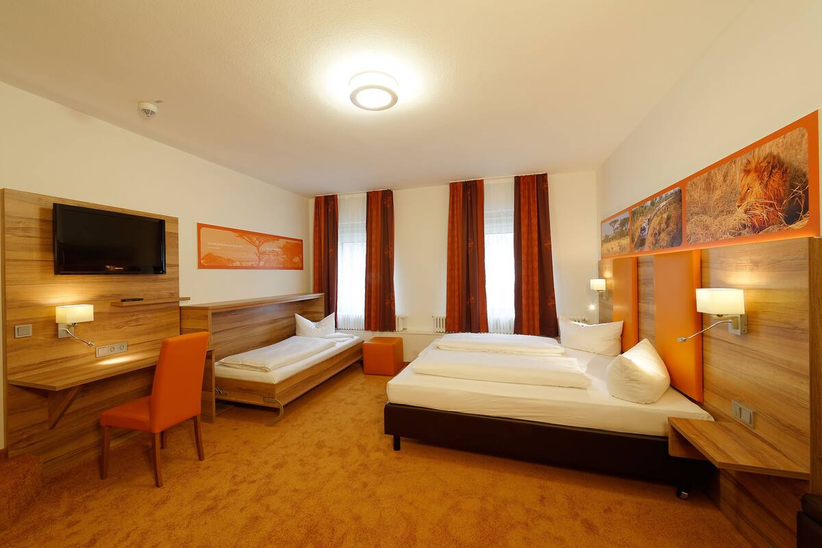 A hotel room with a bed, a desk with a chair, a television, and artwork on the walls.